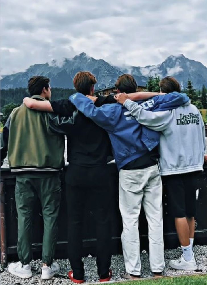 Four friends with arms around each other, standing in front of a mountainous landscape.